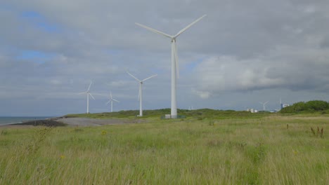 Windmühlen-Drehen-Sich-Durch-Vergilbte-Gräser-Und-Erheben-Sich,-Um-Gras-Zu-Räumen,-Das-Einen-Wolkigen-Sommerhimmel-Zeigt