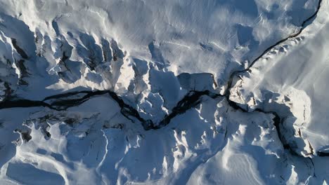 aerial top view of a glacier river flowing through a canyon covered in snow, on a sunny day