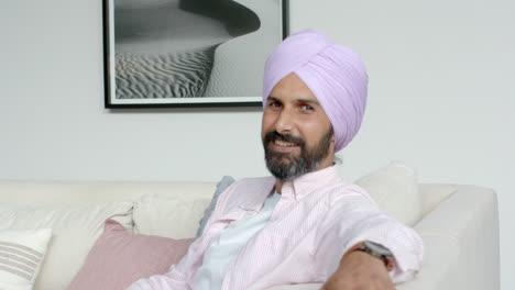smiling man in turban sitting on couch at home, looking relaxed