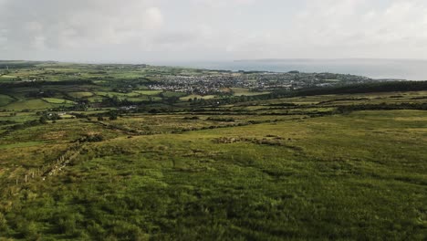 Toma-Panorámica-Aérea-Lenta-De-La-Campiña-Irlandesa-Mirando-Hacia-La-Ciudad-Y-El-Océano