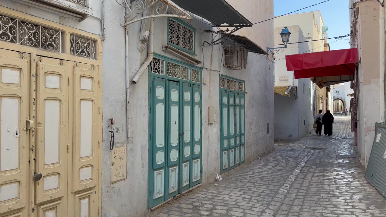 Tunus'un Kayrevan şehrinde Arnavut kaldırımlı bir sokakta yürüyen yayalar.