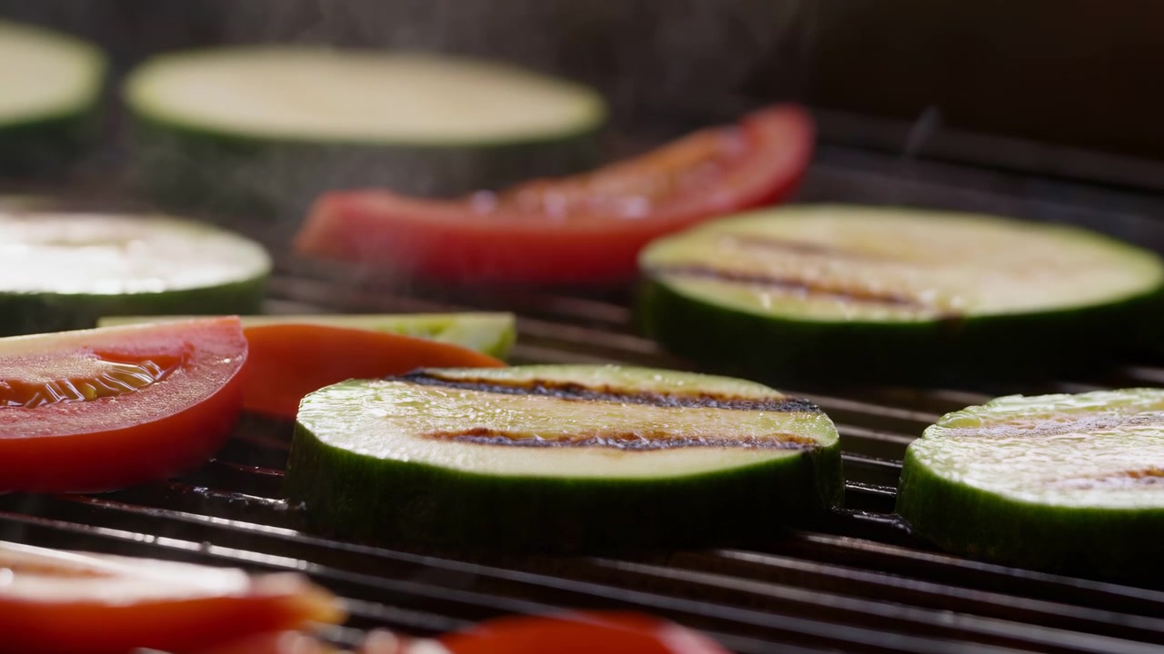 Spesse fette di zucchine e pomodoro rimangono su barre di griglia calde mentre sbuffi di vapore salgono verso l'alto, con una messa a fuoco ridotta che enfatizza le linee scottate e i colori freschi delle verdure
