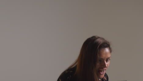 studio shot of excited woman with mobile phone celebrating winning money against grey background