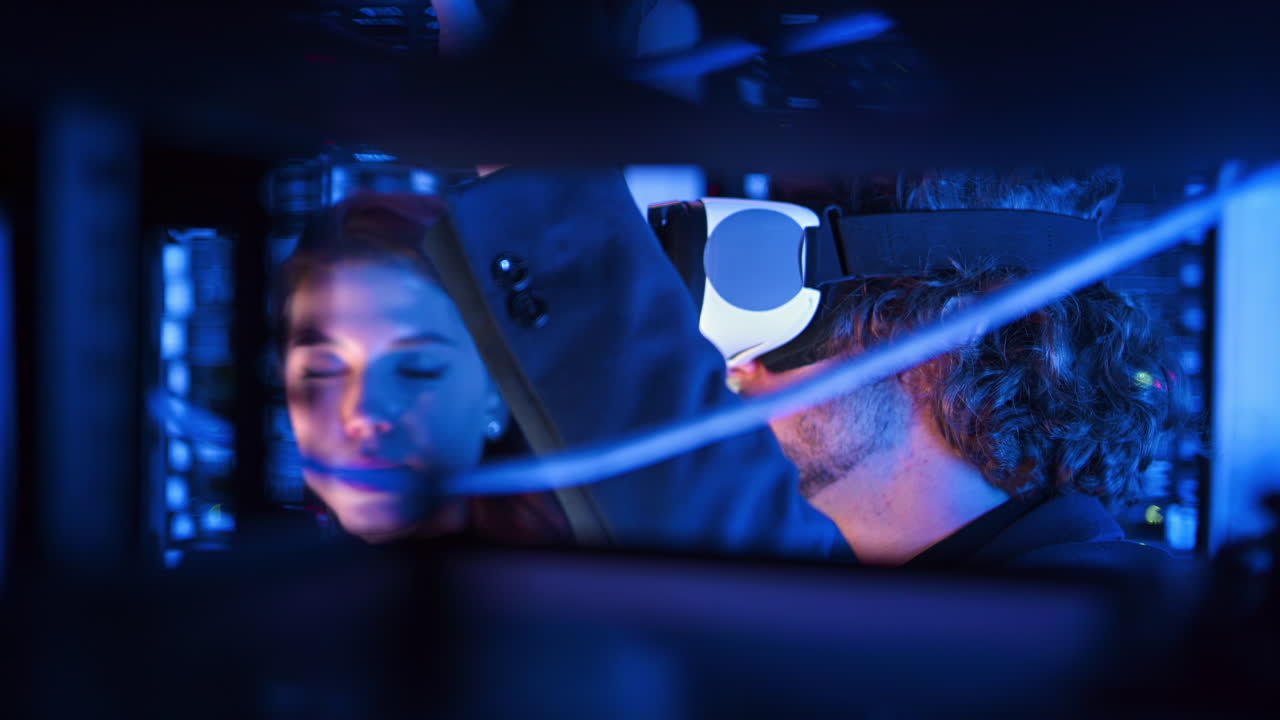 Woman programming in a server room while a man is using a Virtual Reality headset