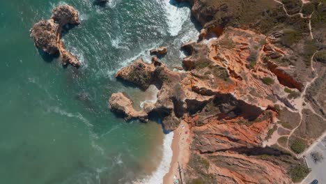 Rugged-red-white-orange-rusted-oceanside-cliffs-bombarded-by-rough-ocean-waves,-algarve-portugal