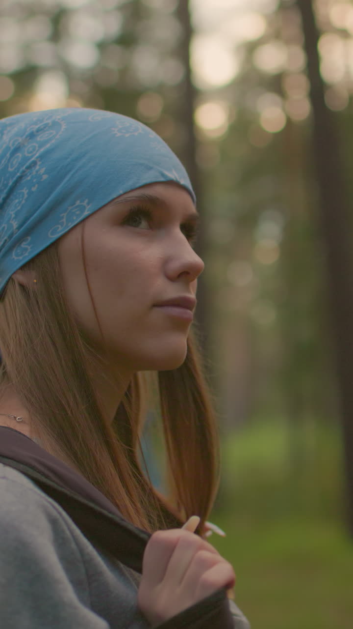 primer plano de damas caminando por un sendero forestal rodeadas de árboles altos, una balancea su bolsa negra sobre su hombro mientras mira cálidamente, mientras que la otra camina a su lado suavemente borrosa en el fondo