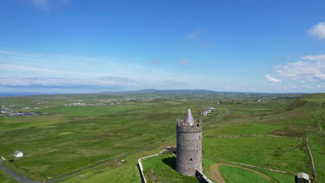 Aerial-Rising-drone-over-Doonagore-Castle-revealing-lush-landscape-with-blue-sky