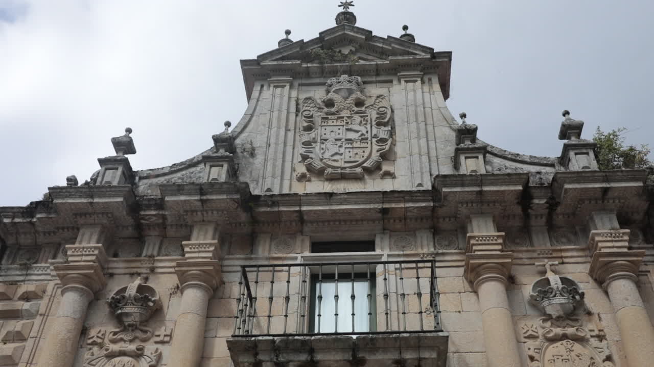 Historic stone facade with intricate carvings and balcony, shot from a low angle under cloudy skies
