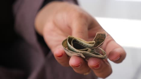 a woman's hand holding a roll of us dollar bills.