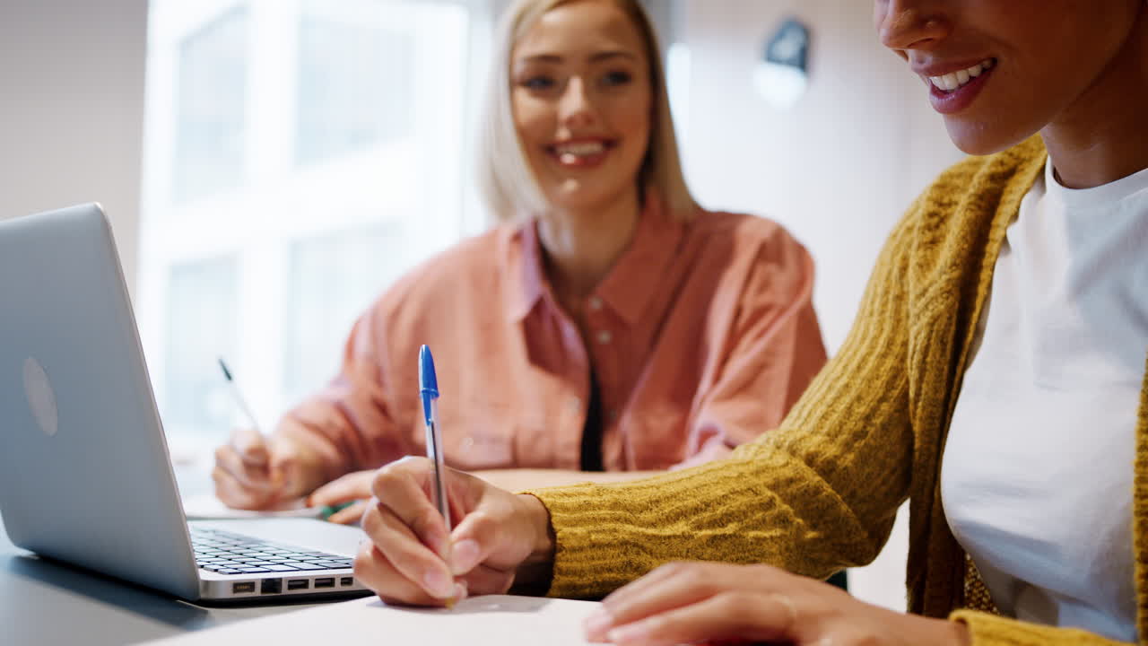 사무실에 앉아 노트북 컴퓨터에서 함께 일하는 두 명의 젊은 여성 크리에이티브의 클로즈업, 선택적 초점, 중간 섹션, 클로즈 업