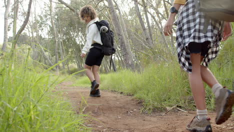 child with curly hair is walking on a dirt path, smiling towards the camera