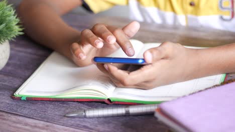 un adolescente usando un teléfono inteligente y un bloc de notas en la mesa ,