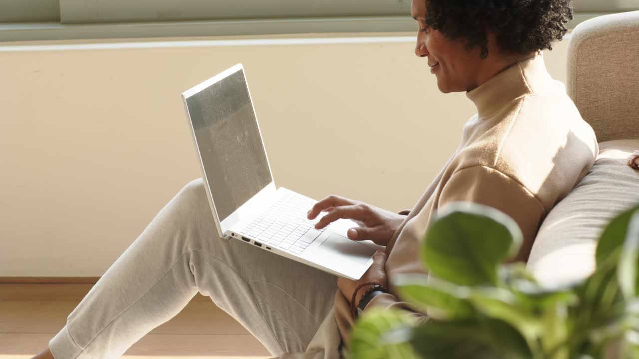 Steadying laptop on lap near window, person is typing keys and glancing outside for work