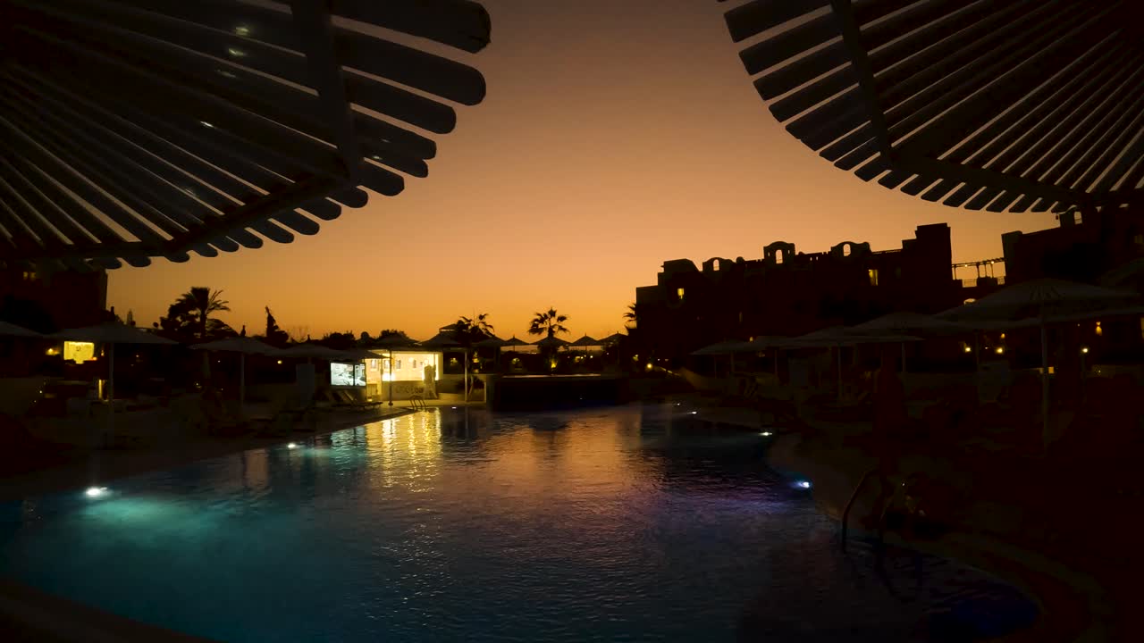 Slow establishing shot of a pool resort under a golden Egyptian sunset