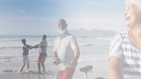 composite of happy diverse senior couple walking with bikes,and dancing on beach