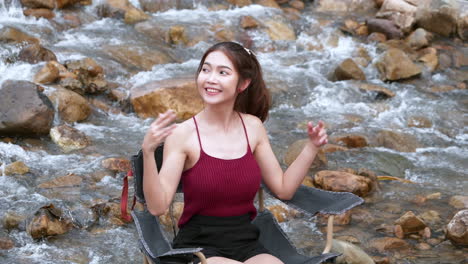 asian woman in red sitting on a chair with big rocks and water slow splashing for relaxing and happiness in the vacation summertime