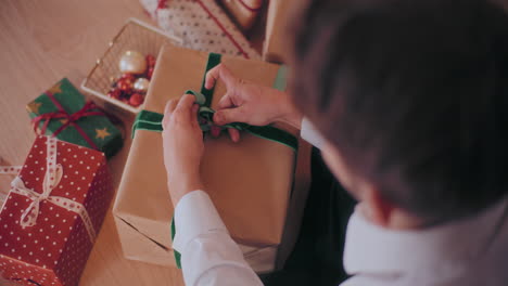 man tying ribbon on wrapped christmas present at home