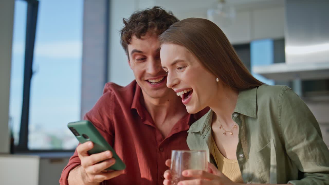 Excited spouses reading message on smartphone breakfasting together home closeup