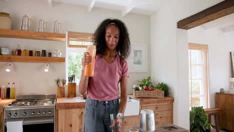 woman pouring fresh juice in kitchen, smiling and enjoying morning, at home