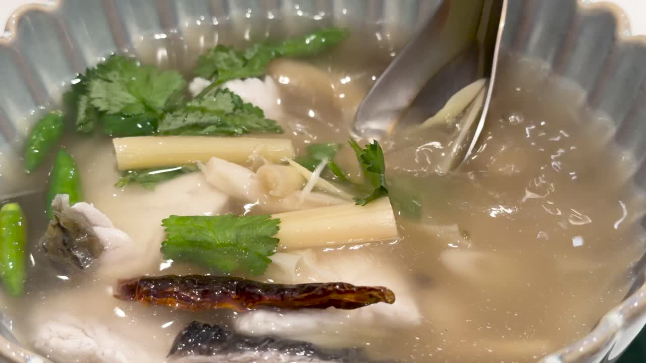 Close-up of Thai tom yum soup with sea bass and herbs, spoon stirring brightly lit