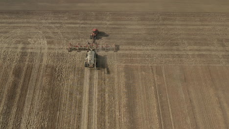 Seeding-Tractor-Working-At-The-Vast-Farmland-In-Saskatchewan,-Canada-On-A-Sunny-Morning---static-drone-shot