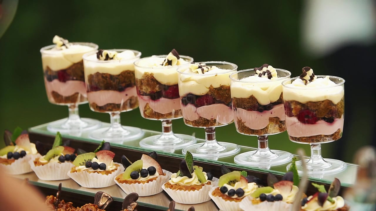 Mano guantata che sistema parfait gourmet e crostatine di frutta su un buffet di dolci