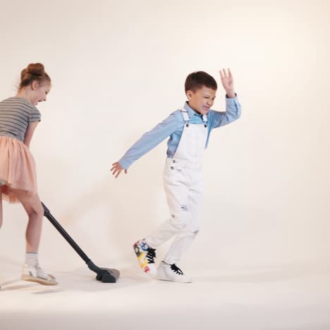 little boy is running away from the girl with a vacuum cleaner in her hands. funny kids are playing while cleaning