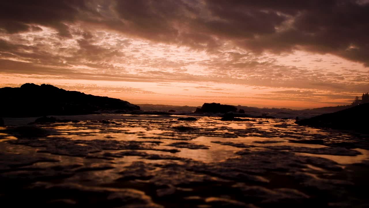 el agua de la piscina de rocas regresa al océano, cielo dorado con una puesta de sol de fuego