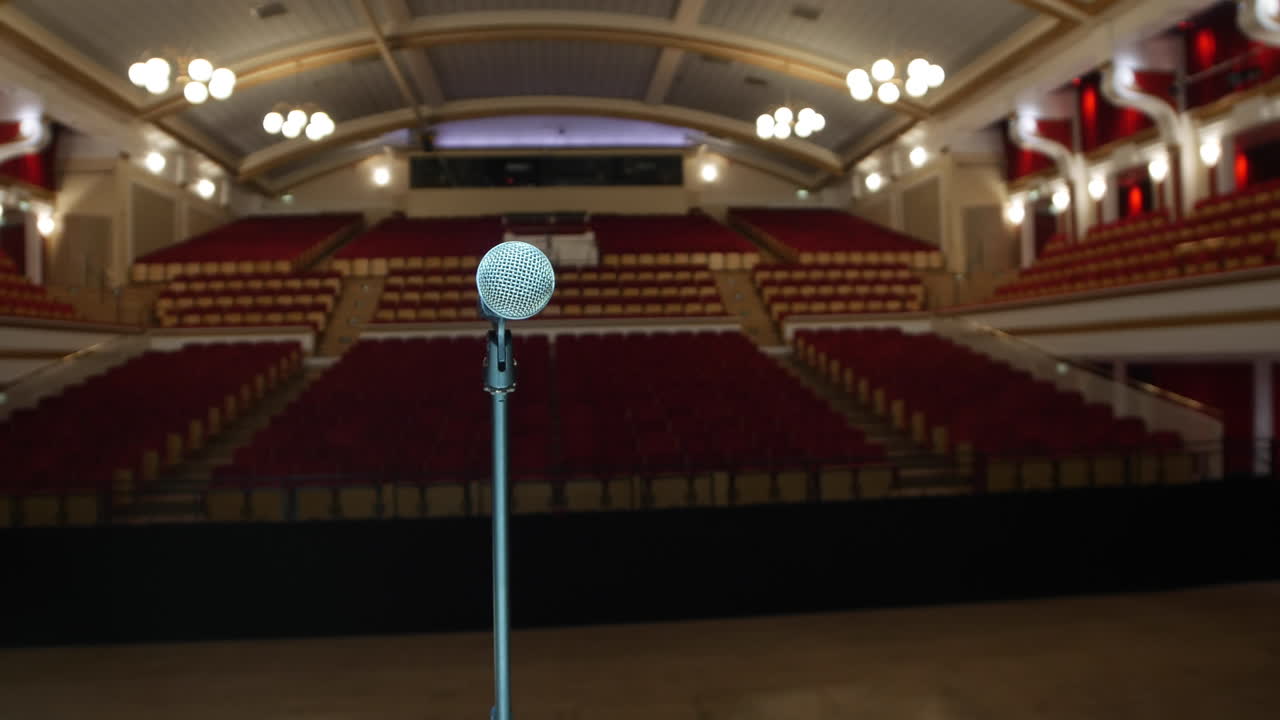 un micrófono a la luz de un soporte de micrófono en un escenario grande en un teatro vacío