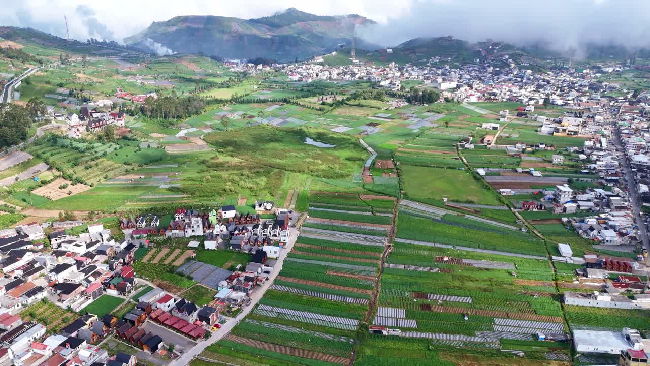 Beautiful panoramic shot of cultivated farmlands and a mountain town under a clear blue sky. Aerial footage showcasing rural life, agriculture, and natural scenery in the highlands
