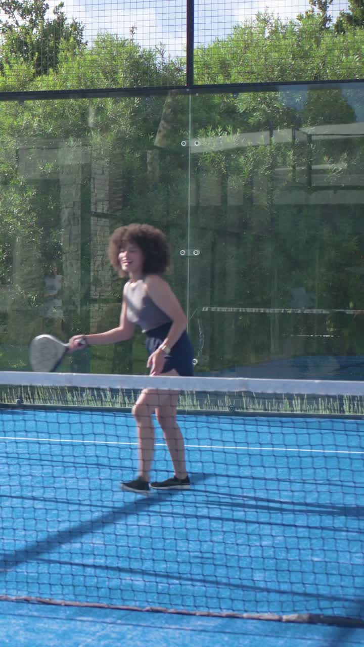 Donna che si sposta per prendere la palla in arrivo, colpendo con la racchetta vicino alla rete su un campo da padel in allenamento.