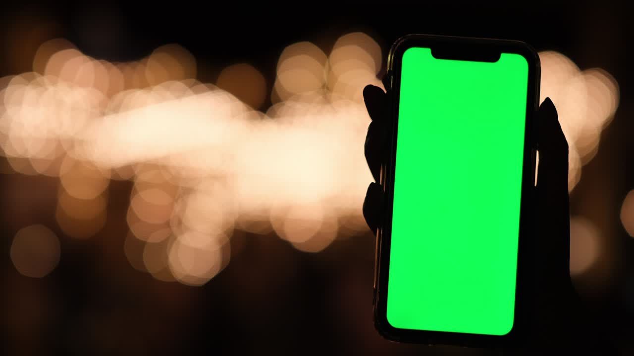 hand holding green screen smart phone at night. Golden bokeh background