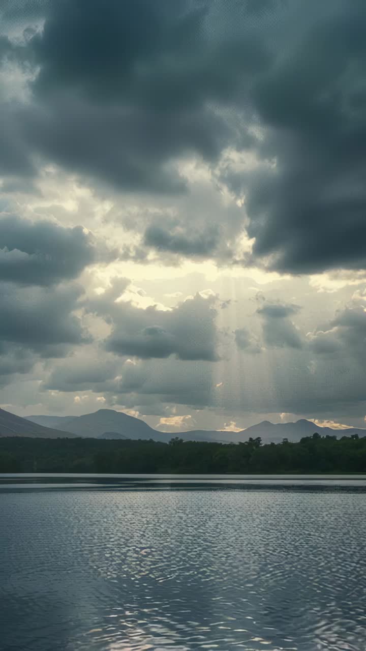 Vertical video: Shifting cloud layer forming gap, sending sunbeams reflecting on lake and hills