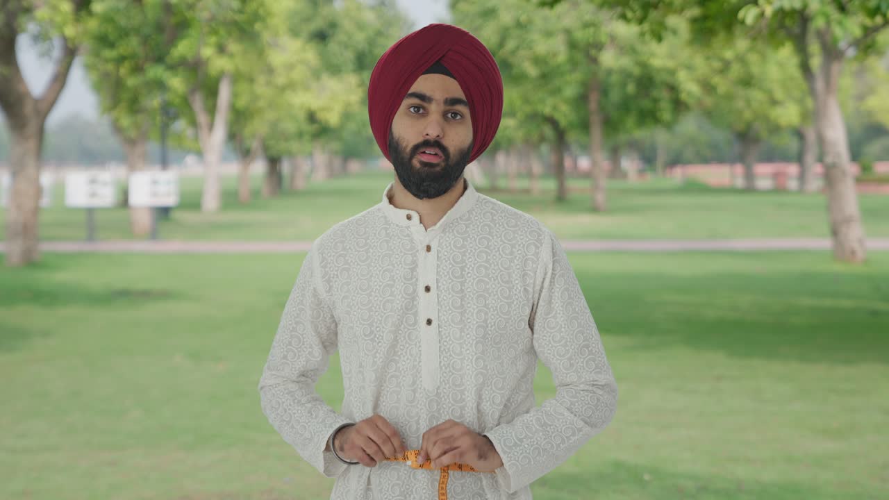 Pria Sikh India yang sedih mengukur lingkar pinggang menggunakan meteran di taman.