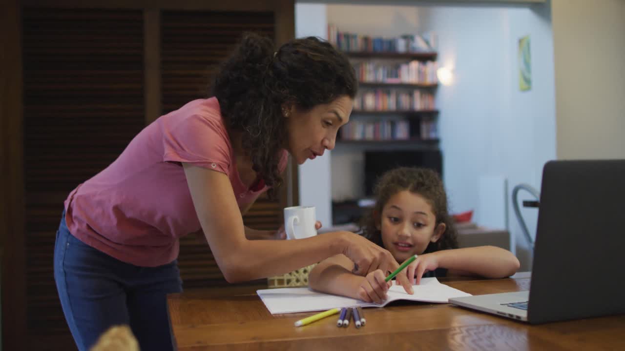 madre e hija de raza mixta felices haciendo la tarea juntos en casa