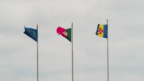 flags of eu, portugal and madeira island swaying at gentle breeze. medium shot