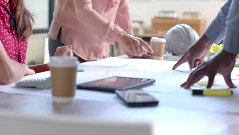 midsection of diverse architects discussing blueprints on table in office, slow motion