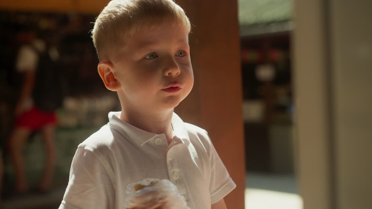 빛의 빛은 은 날에 반죽으로 소시지를 먹는 소년에게 떨어집니다. 가운 셔츠를 입은 놀란 아이는 오두막집의 마당에서 은 소시지를 은 후 에 손가락을 니다.