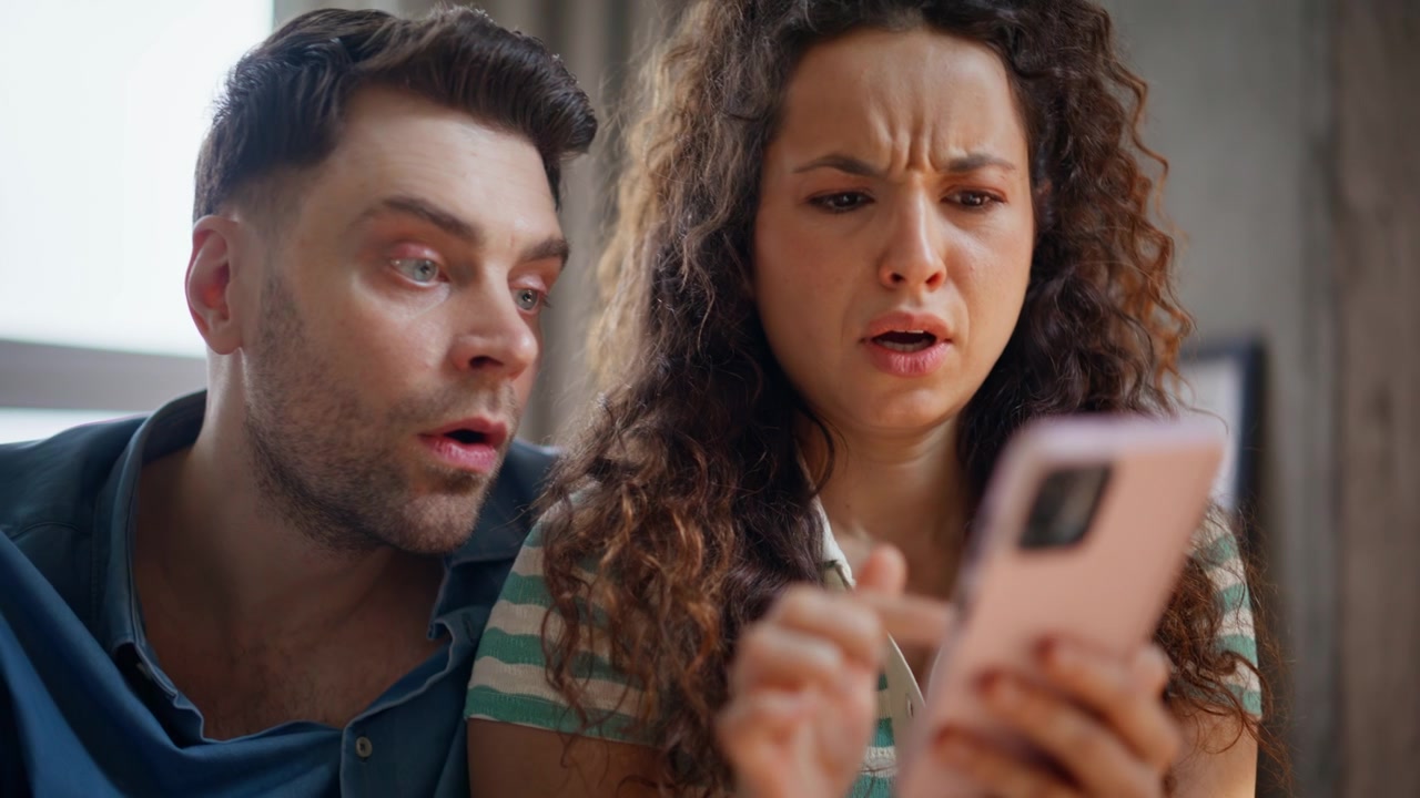 Casal chocado lendo notícias no smartphone. Homem e mulher surpresos reagindo em close-up.