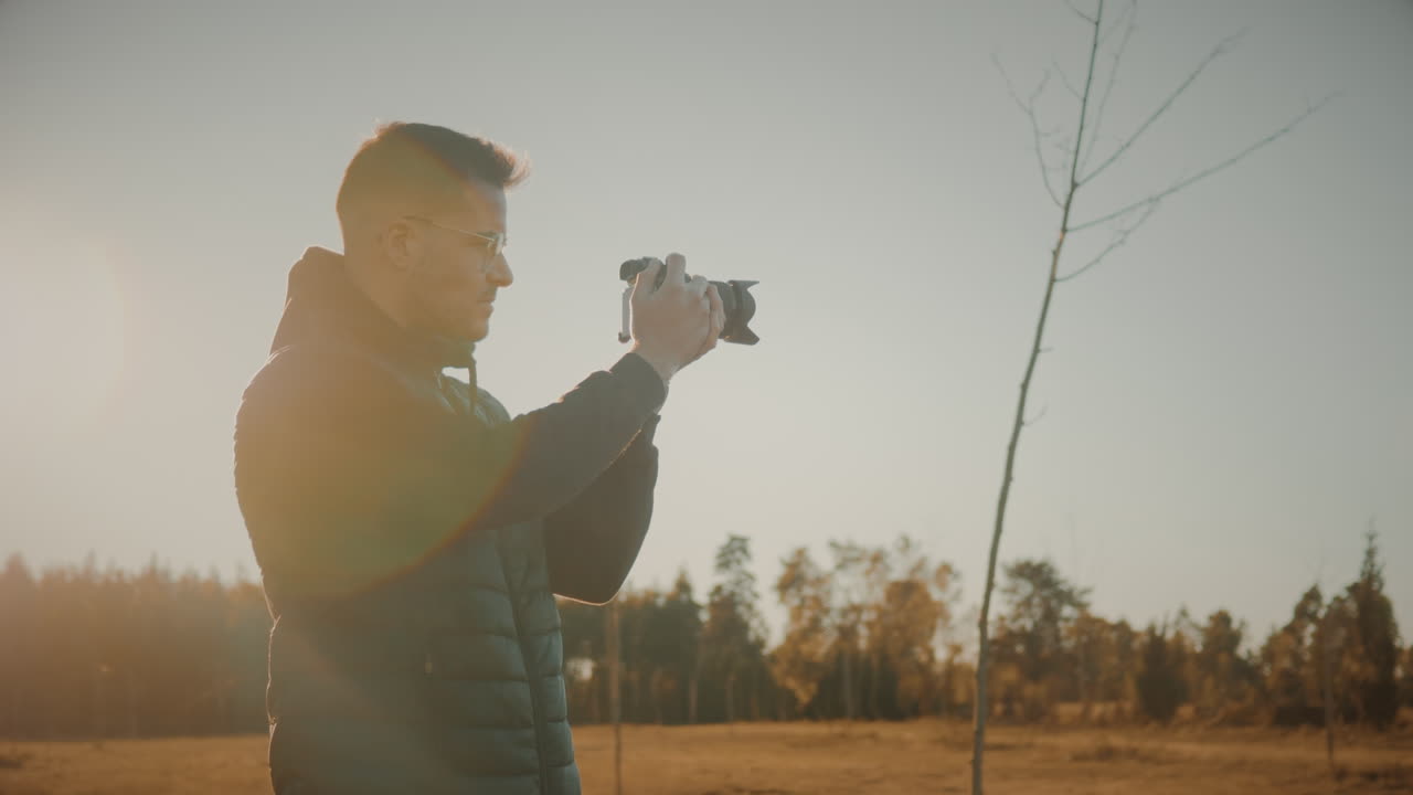 Mandlig fotograf alene på åben mark ude i naturen ved solnedgang