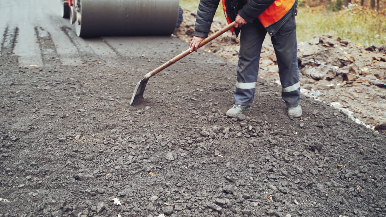 Workers in uniform with shovels during road street repairing works. Street resurfacing. Fresh asphalt construction. Close-up