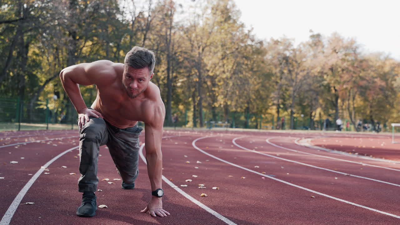 Bearded sportsman on a sports track. Handsome man with muscular body exercising outdoors on the stadium. Sprinter runner preparing for run.