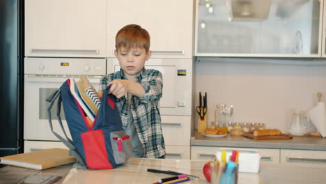 boy packing backpack in kitchen