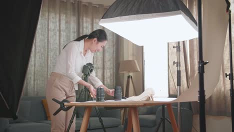 asian female photographer changing camera's lens while taking photos of women's shoes in home studio