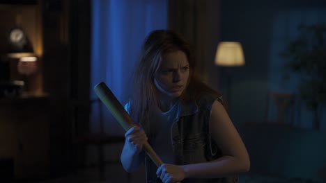 tense young woman holding baseball bat in a dark home