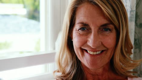 Portrait-of-happy-senior-woman-standing-next-to-window