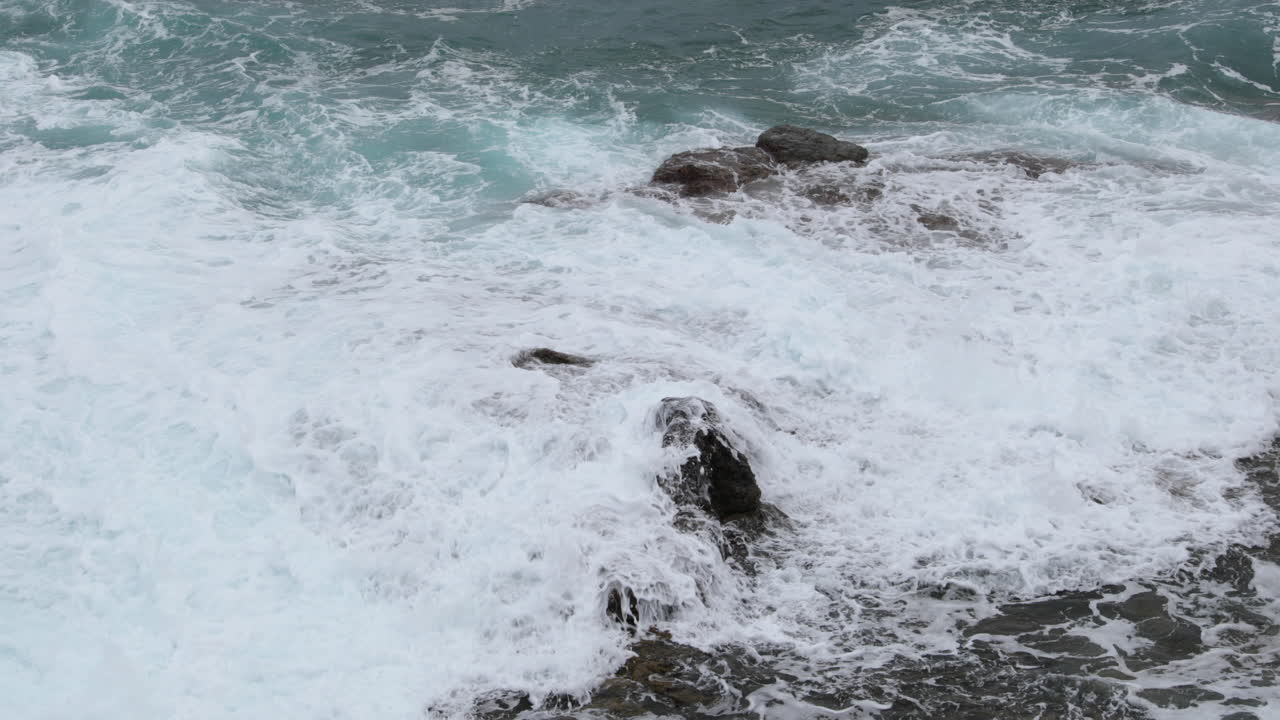 Sea water during a tide crashing strongly into a stony shore full of obstacles and hitting rocks the water, then decomposes to a high incidence 4k slow motion capture at 60fps