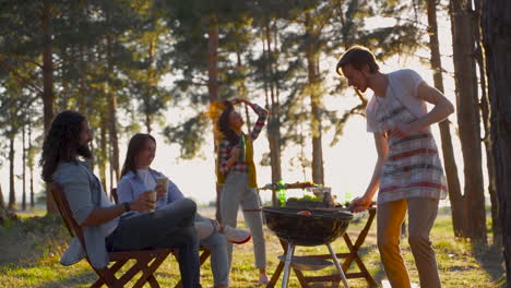 mujeres y hombres jóvenes cocinando una barbacoa y bailando en el campo. personas disfrutando de un picnic en la naturaleza.