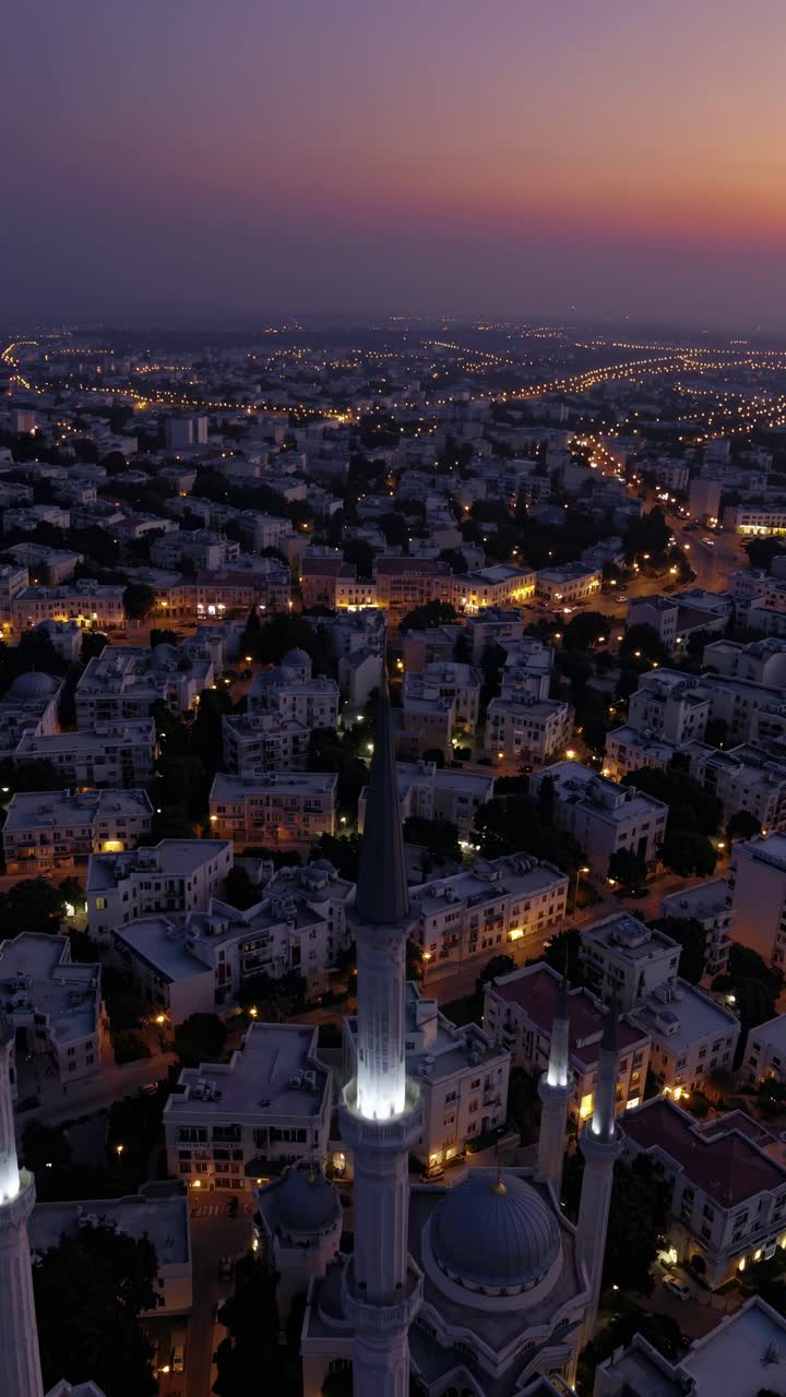 Four minarets of a grand mosque rise above a sprawling cityscape, bathed in the warm glow of sunset, creating a breathtaking scene of urban beauty and spiritual significance