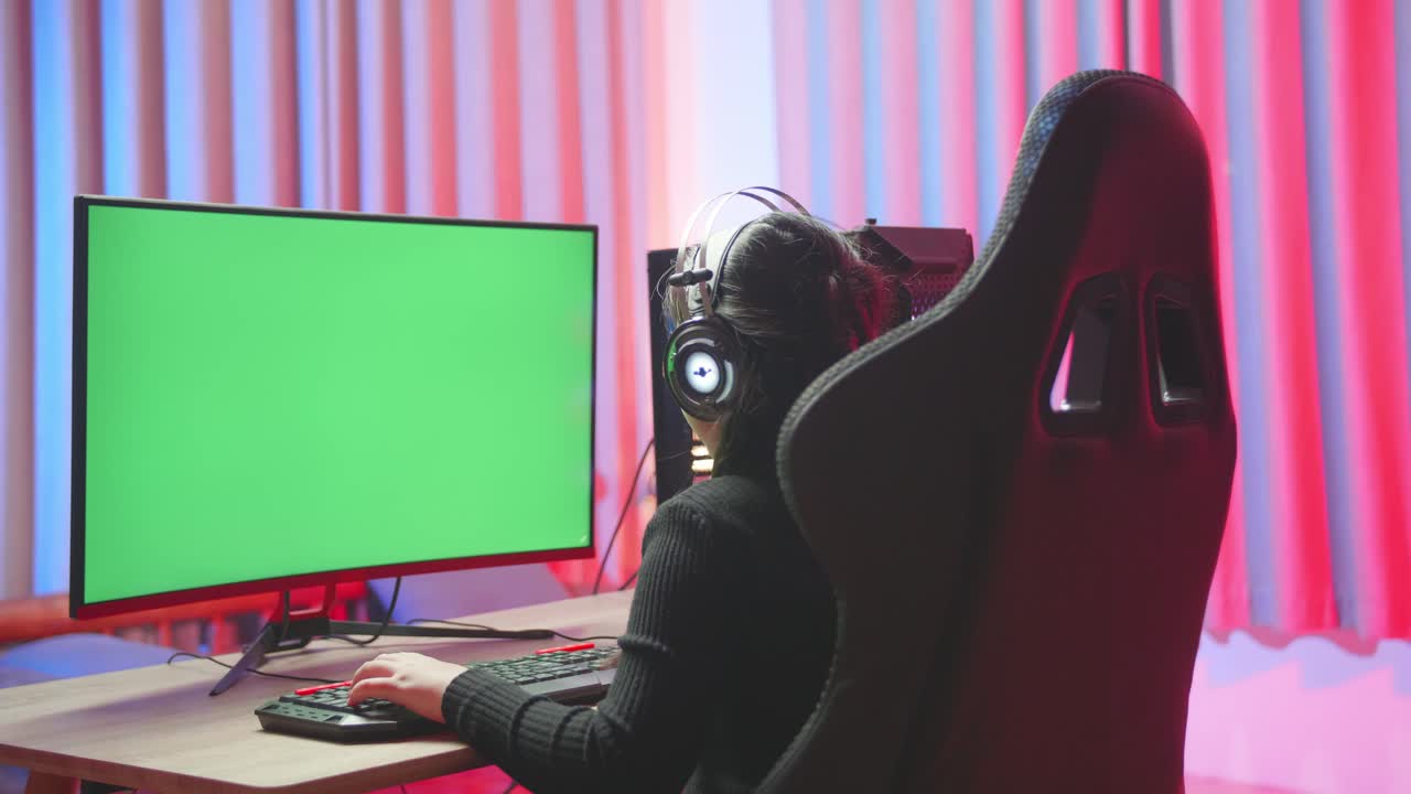Young Girl Seating In Front Of The Computer While Playing Exited Computer Game With Green Screen Display